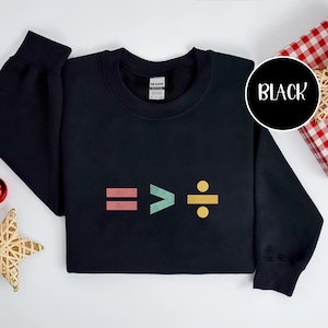Könnte beinhalten: Schwarzes Sweatshirt mit bunten mathematischen Symbolen: ein Gleichheitszeichen, ein Größer-als-Zeichen und ein Divisionssymbol. Das Wort "BLACK" steht in weißer Schrift in einem schwarzen Kreis. Das Sweatshirt ist von der Marke Gildan.