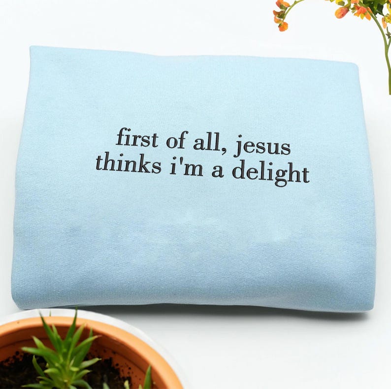 Pu&ograve; includere: Una felpa azzurra con la scritta nera "first of all, jesus thinks i'm a delight". La felpa piegata sembra essere realizzata in un materiale morbido. Lo sfondo &egrave; bianco.
