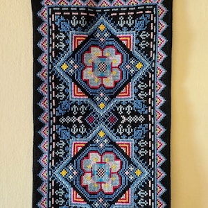 May include: A black tapestry with a geometric pattern in shades of blue, pink, yellow, and red. The pattern features stylized flowers and intricate details.