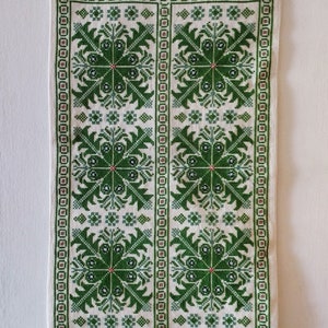 Könnte beinhalten: Ein weißer Wandteppich mit grünen gestickten Blumenmustern. Der Wandteppich hängt an einer Holzstange mit grünen und silbernen Perlen, die von unten herabhängen.