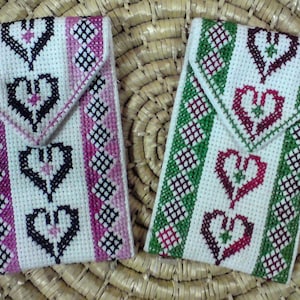 May include: Two small white fabric pouches with embroidered hearts and geometric patterns. One pouch has pink and black embroidery, the other has green and red embroidery.