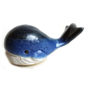 May include: A ceramic whale ornament in blue and white. The whale has a dark blue top, a lighter blue body, and a white underbelly. The tail is black. The figurine is a decorative item.