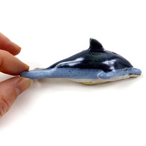 May include: A ceramic dolphin figurine with a blue and white glaze. The dolphin is swimming to the right.