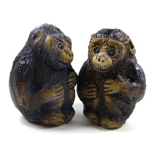 May include: Two small brown ceramic monkey figurines, each in a seated pose with a slightly different facial expression. The monkeys are looking at each other.