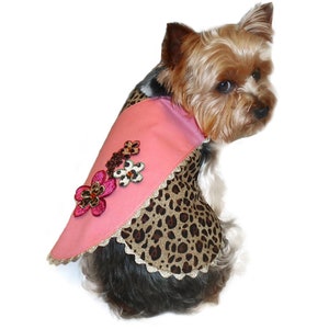 May include: A pink dog shirt with a leopard print design and floral embellishments. The shirt has a scalloped edge and is worn by a small dog.