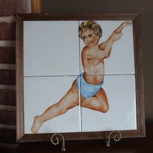 May include: A framed tile set with a hand-painted image of a young boy in a blue swimsuit, with a white background.