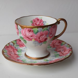 May include: A white teacup and saucer set with a pink and gold floral design. The cup has a delicate handle and a wide rim. The saucer has a matching floral pattern.