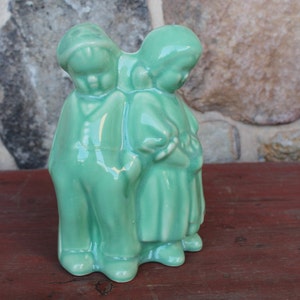 Könnte beinhalten: Eine antike Keramikfigur eines Paares, das nebeneinander steht. Die Figur ist in einem hellgrünen Glasurton bemalt und zeigt einen Mann und eine Frau in traditioneller Kleidung.