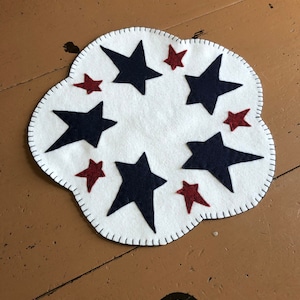 May include: A white felt table runner with a scalloped edge, featuring a circle of navy blue and red felt stars.