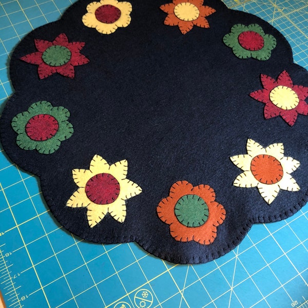 Black table mat/ candle mat measuring 18 inches across with red, orange yellow and green flowers.
