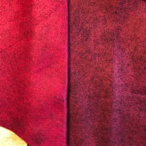 May include: Two pieces of burgundy felt fabric, one folded in a triangle shape and the other flat. The fabric has a textured surface.