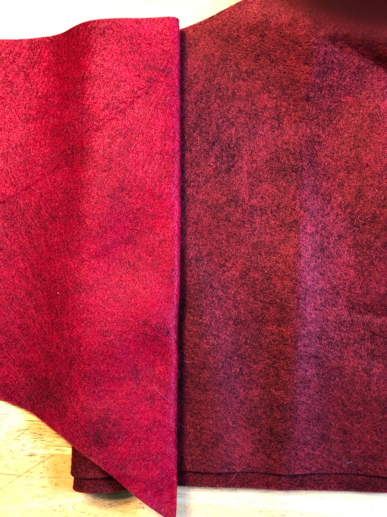 May include: Two pieces of burgundy felt fabric, one folded in a triangle shape and the other flat. The fabric has a textured surface.
