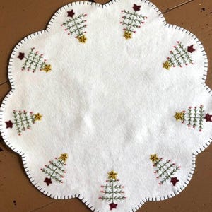Primitive feather tree candle mat with an off white background and green feather trees in the scallops.