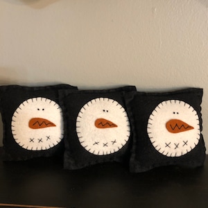 Snowman bowl filler pillows set of 3 with a black background and off white snowman faces . Measuring 5 inches square.