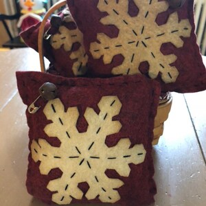 Bowl filler snowflake pillows measuring 5” square with a dark red background and coffee dye white snowflakes.