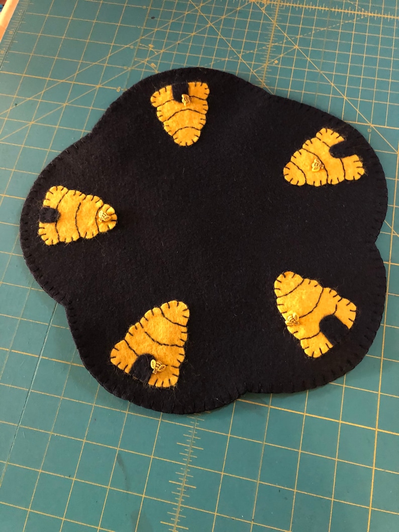Bee candle mat measuring 12 inches across black background with bee skeps in each scallop with a bee button on each skep