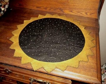 Table topper/candle mat shaped like a sunflower. It measures 18" across made from gold wool felt blend with a black center.