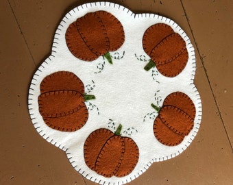 Pumpkin candle/table mat with an off white background and orange pumpkins in the scallops