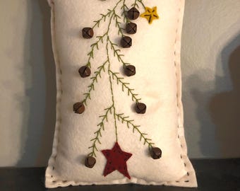 Primitive pillow with a feather tree and bells on the branches .