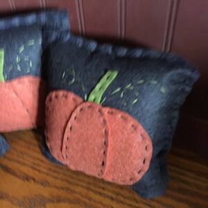 May include: Two felt pumpkins with orange felt faces and green felt stems. The pumpkins are sewn onto a dark blue felt background.