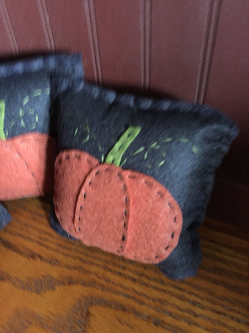 May include: Two felt pumpkins with orange felt faces and green felt stems. The pumpkins are sewn onto a dark blue felt background.