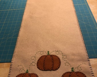 Primitive pumpkin table runner with a tan background measuring 12x36 inches with 3 small pumpkins on each end