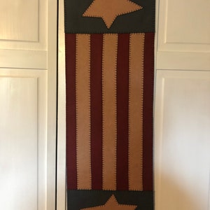 May include: A patriotic table runner with a red, white, and blue color scheme. The runner features a large star in the top section and a smaller star in the bottom section. The middle section features alternating red and white stripes.
