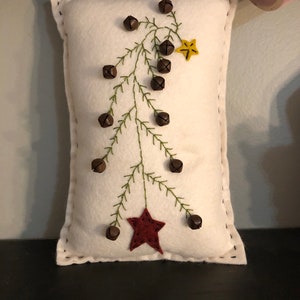 Primitive pillow with a feather tree and bells on the branches .