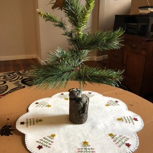 Tree skirt (hole in center)with off white background and feather trees in the scallops measuring 18 inches diameter.