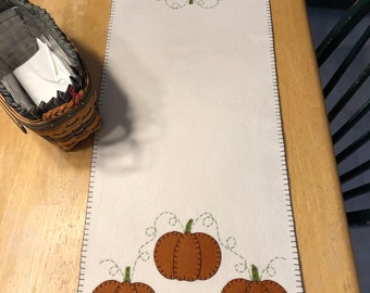Primitive pumpkin wool felt blend table runner with an off white background measuring 12x36 inches with 3 small pumpkins on each end