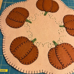 Pumpkin candle/table mat with a tan background and orange pumpkins in the scallops