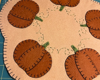 Pumpkin candle/table mat with a tan background and orange pumpkins in the scallops
