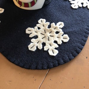 May include: A dark blue felt snowflake table runner with white felt snowflakes. The runner has a stitched edge.