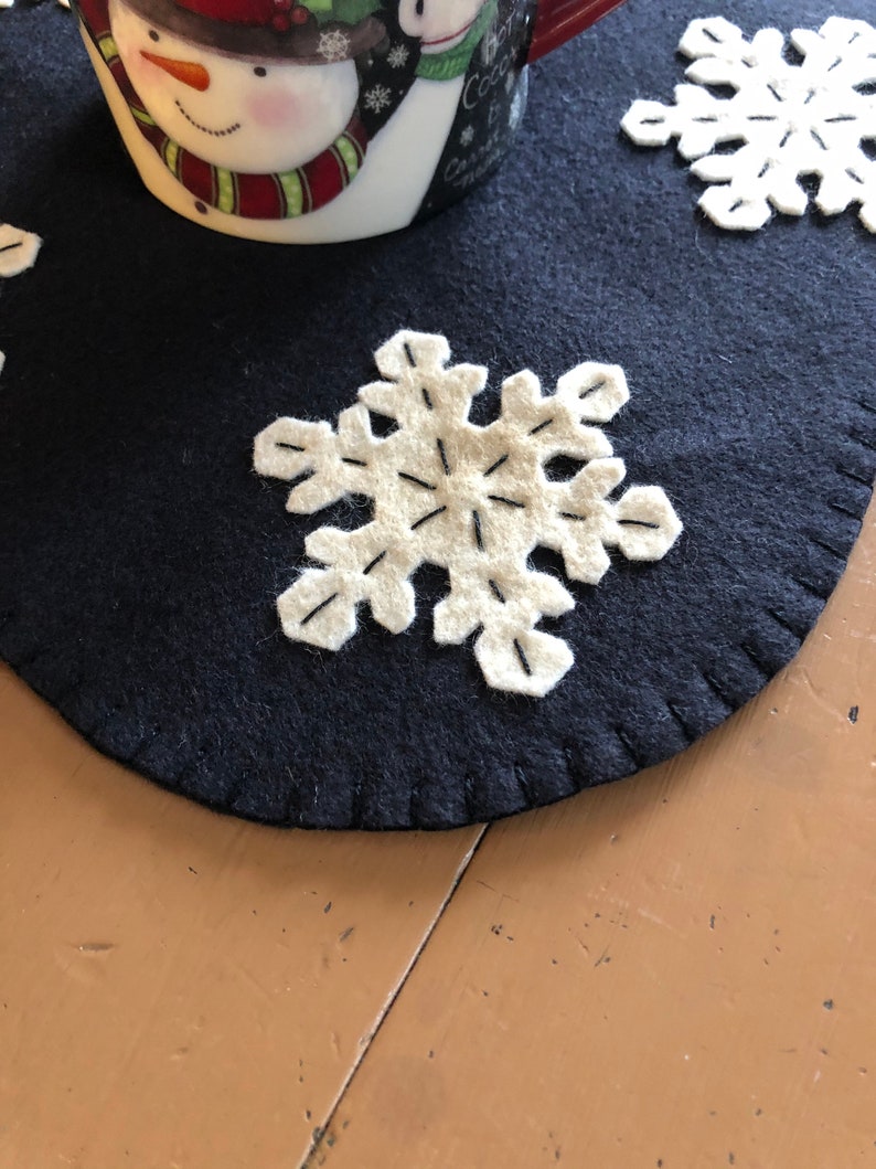 May include: A dark blue felt snowflake table runner with white felt snowflakes. The runner has a stitched edge.