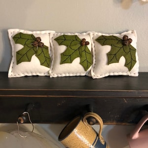 Bowl filler holly pillow with an off white background, 3 green holly leaves and 3 rusty bells. Set of 3.