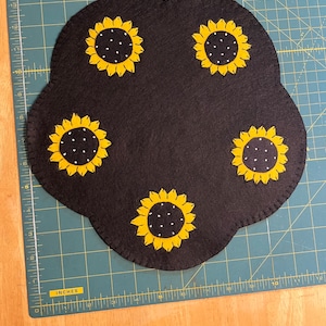 Table topper/candle mat with sunflowers in each of 5 scallops on a black background measuring 12 inches across