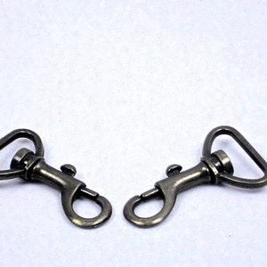May include: Two antique gold-toned metal swivel clasps with a spring-loaded gate. The clasps are designed for attaching to straps, bags, or other items.