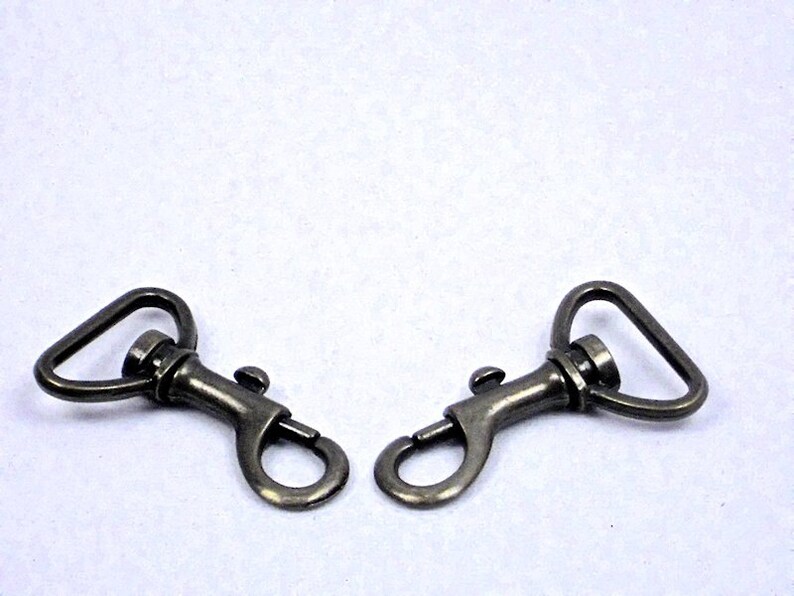 May include: Two antique gold-toned metal swivel clasps with a spring-loaded gate. The clasps are designed for attaching to straps, bags, or other items.