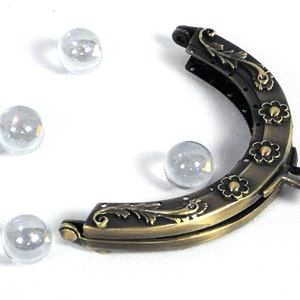 May include: A brass-colored purse frame with a floral design and a latch closure. The frame is open and has a half-circle shape.