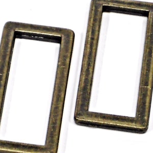 May include: Two rectangular metal rings with a bronze finish. The rings are open in the center and have a slightly worn appearance. They are likely used for crafting or jewelry making.