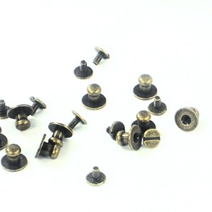 May include: A collection of antique gold-toned metal furniture knobs with screws. The knobs have a round base and a raised dome-shaped top.