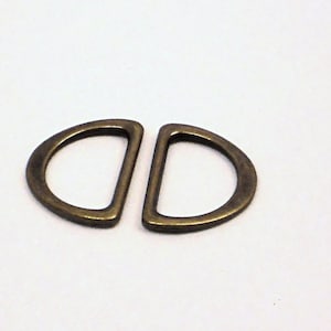 May include: Two antique gold-toned metal D-rings, each with a half-circle shape, are shown against a white background.