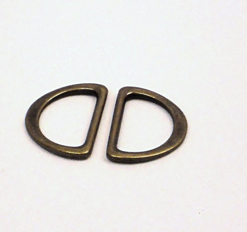 May include: Two antique gold-toned metal D-rings, each with a half-circle shape, are shown against a white background.