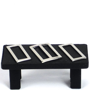May include: Three silver metal rectangular slider buckles on a black display stand.