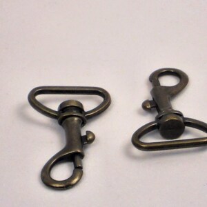 May include: Two antique brass swivel clasps with a D-ring and a hook. The clasps are a common hardware finding for bags, purses, and other leather goods.