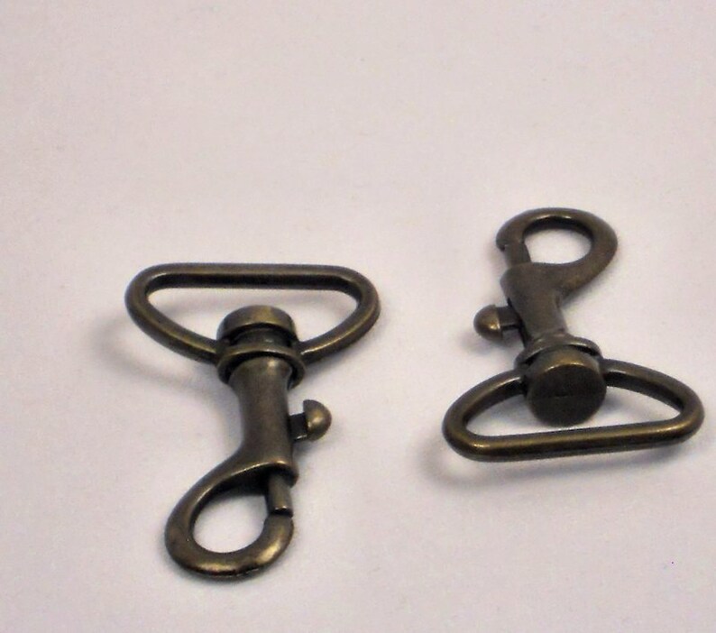 May include: Two antique brass swivel clasps with a D-ring and a hook. The clasps are a common hardware finding for bags, purses, and other leather goods.