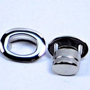 May include: A set of two silver metal grommets, one with a raised lip and the other with a flat surface. The grommets are used for attaching fabric or other materials to a surface.