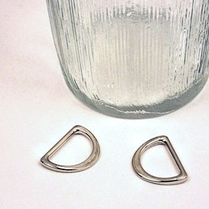 Puede incluir: Dos anillos en D plateados, tambi&eacute;n conocidos como anillos en D o anillos en forma de D, se muestran sobre una superficie blanca. Los anillos tienen un di&aacute;metro de aproximadamente 2,5 cm.