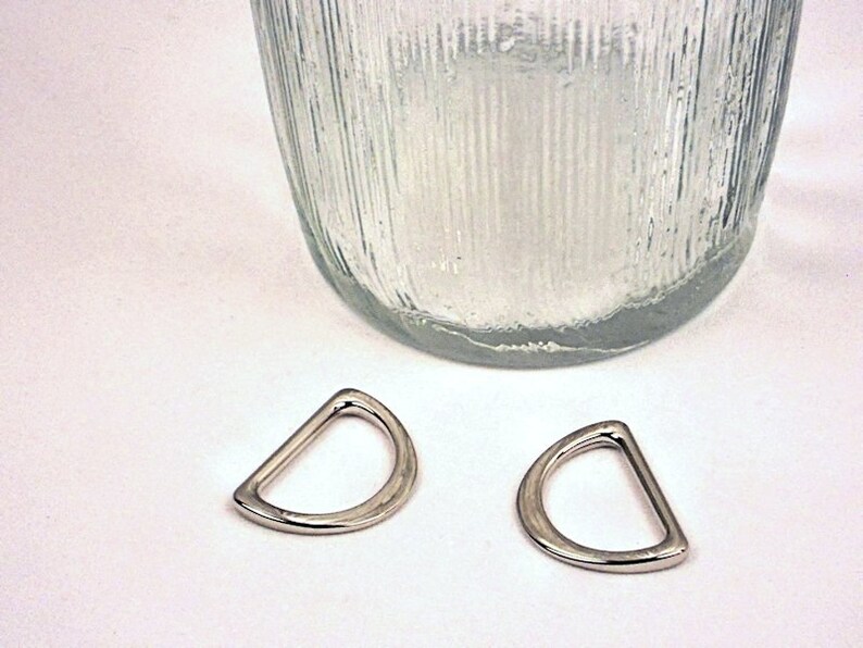 Puede incluir: Dos anillos en D plateados, tambi&eacute;n conocidos como anillos en D o anillos en forma de D, se muestran sobre una superficie blanca. Los anillos tienen un di&aacute;metro de aproximadamente 2,5 cm.