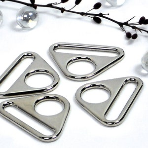 May include: Four silver triangular metal rings with a D-shaped opening. The rings are smooth and shiny.